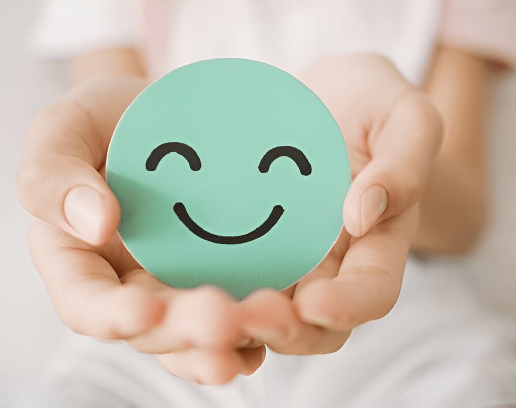 Hands holding a green smiley face cutout symbolizing happiness and well-being.